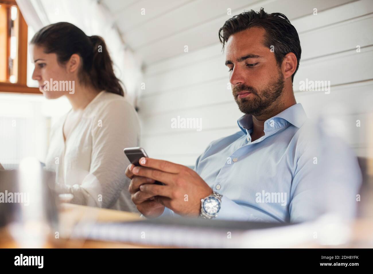 Mittelerwachsener Geschäftsmann mit Mobiltelefon von einer Kollegin in Büro Stockfoto