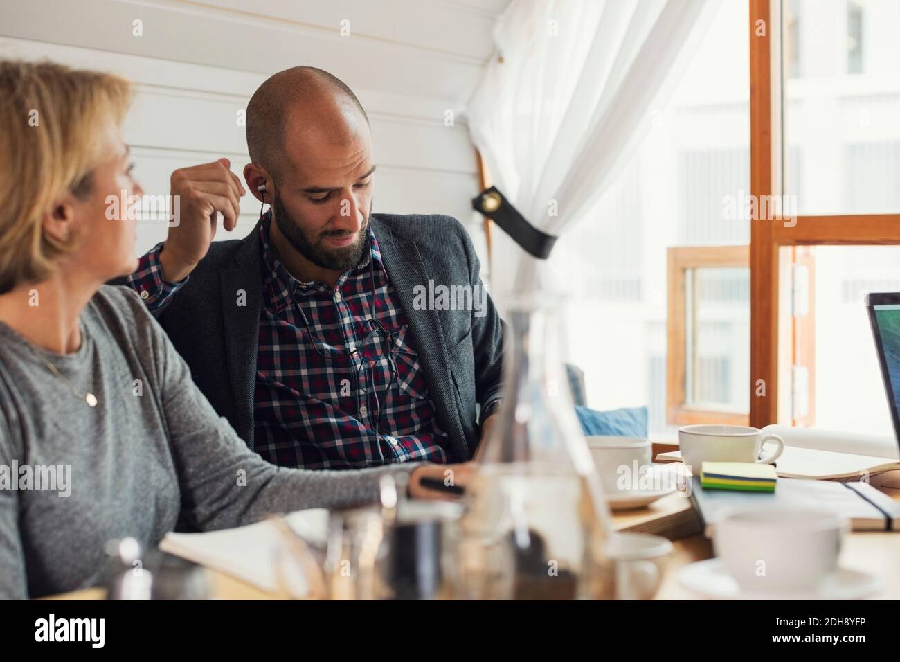 Mittelerwachsener Geschäftsmann, der Ohrhörer trägt, während er neben einer Frau sitzt Kollege im Büro Stockfoto