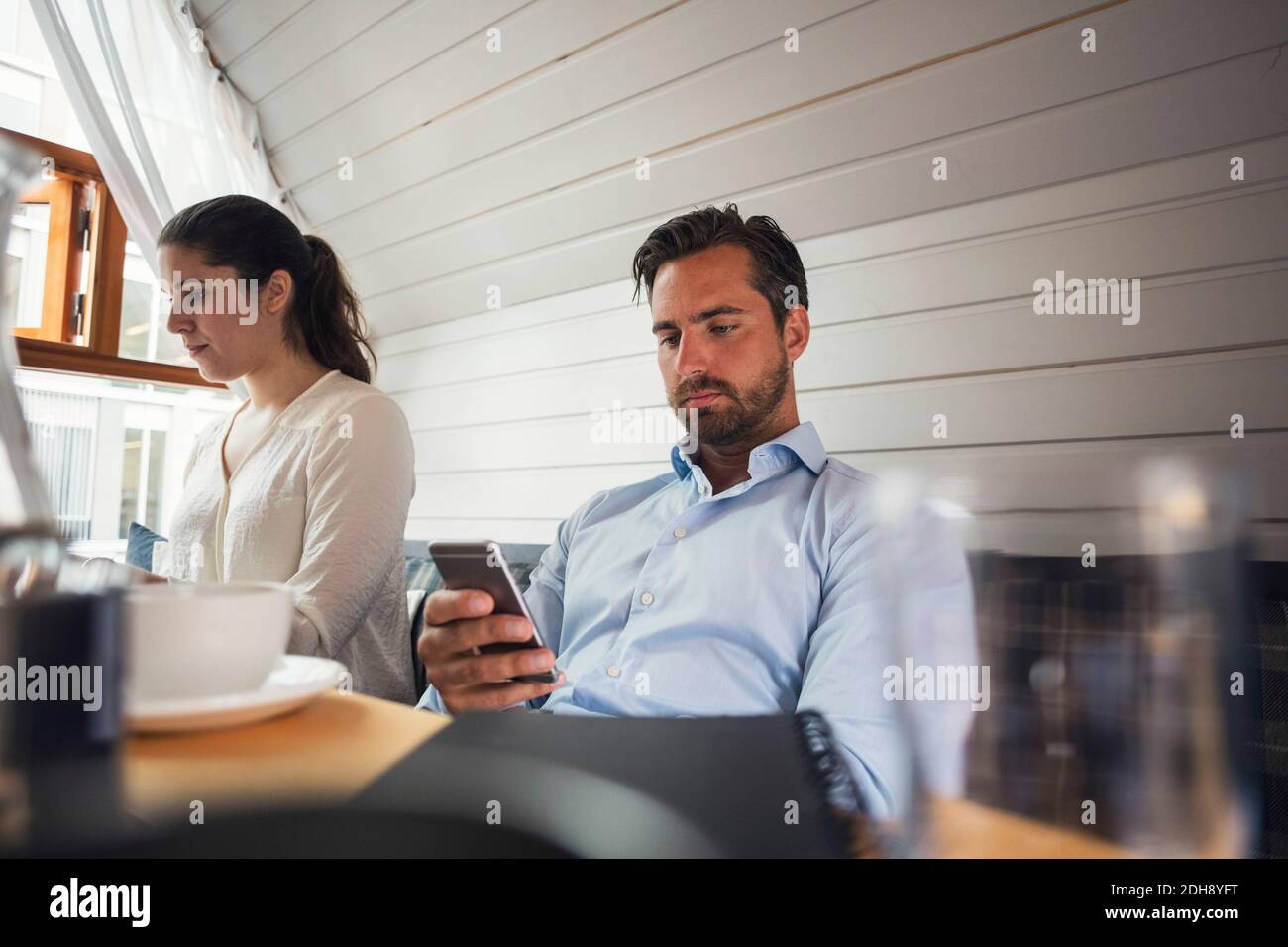 Mittelerwachsener Geschäftsmann mit Smartphone von weiblichen Kollegen in Büro Stockfoto