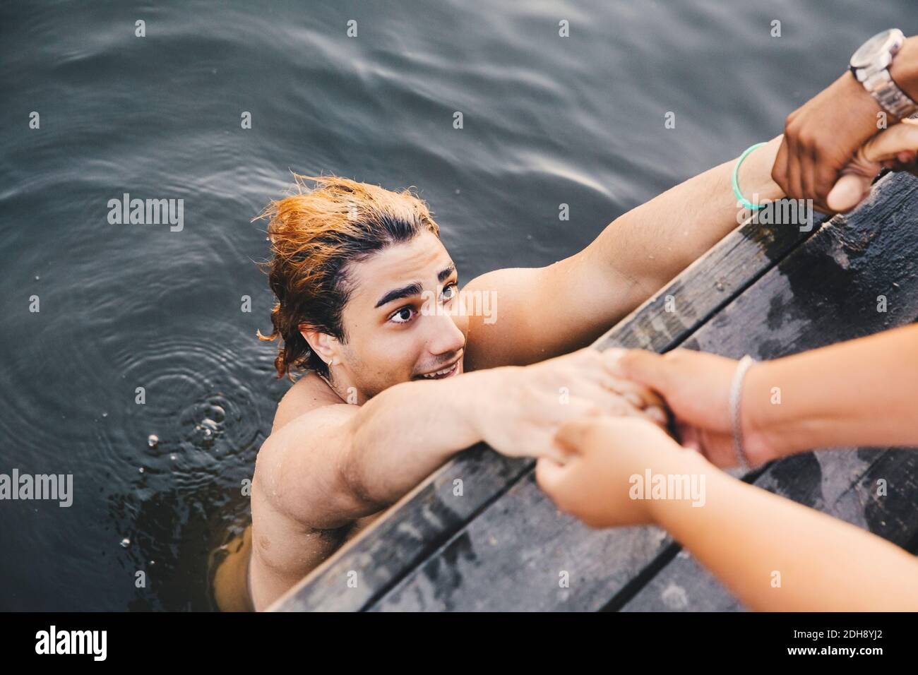 Zugeschnittenes Bild von männlichen Freunden, die Hände mit jungen Mann halten Im See Stockfoto