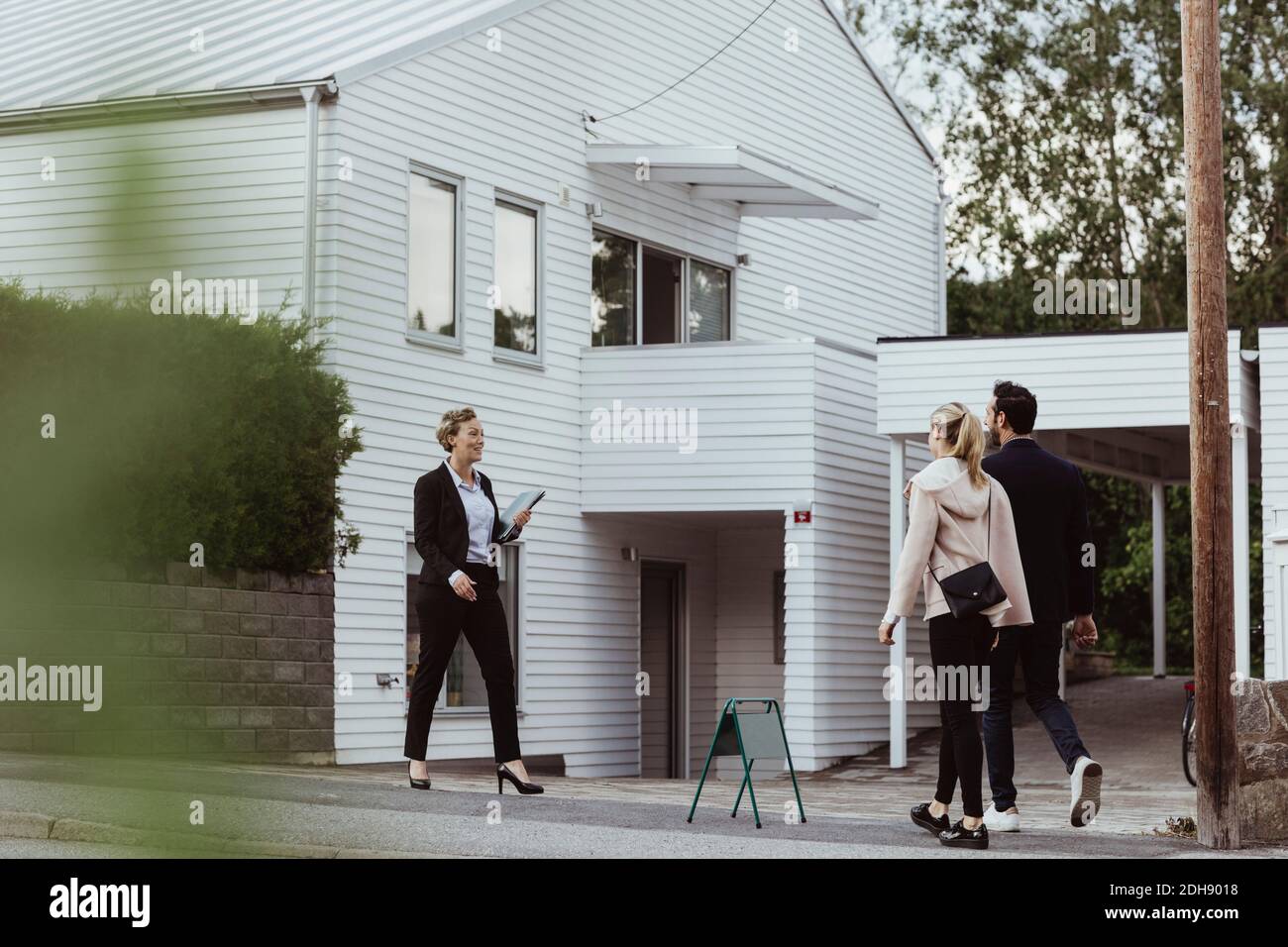 Lächelnder Immobilienprofi im Gespräch mit einem Paar außerhalb des neuen Hauses Stockfoto