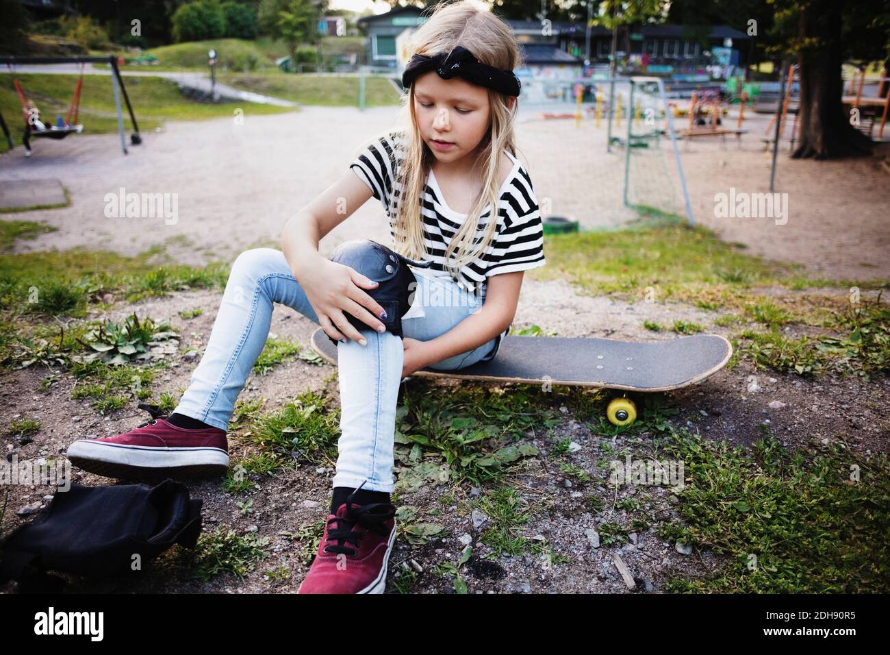 Mädchen binden kniepad während sitzen auf Skateboard im Park Stockfoto