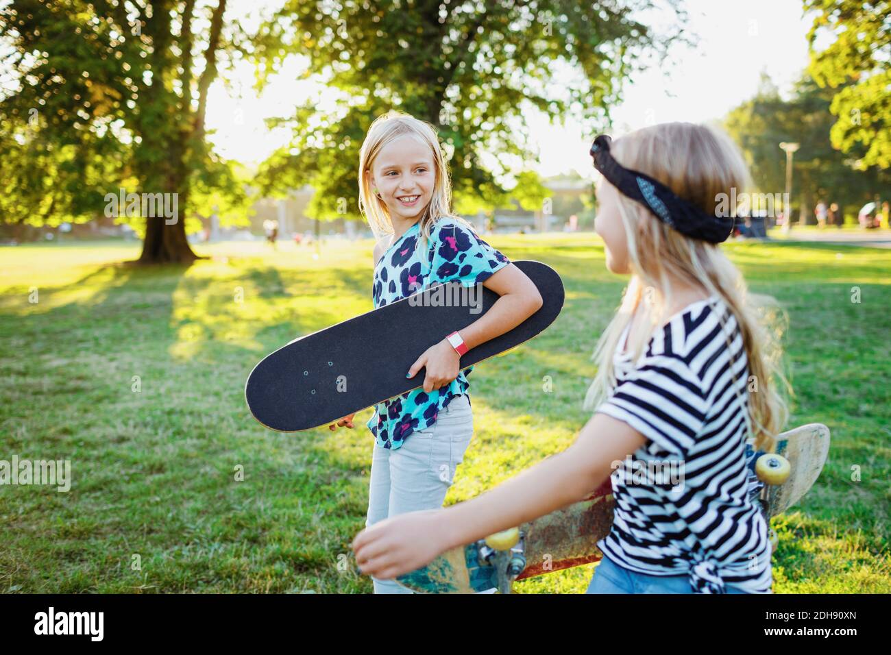 Lächelnde Freunde tragen Skateboards zu Fuß auf Gras Feld Stockfoto