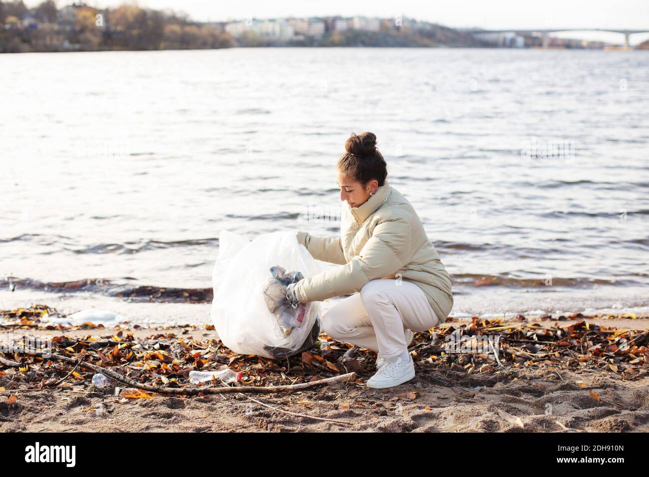 Junge Umweltschützerin sammelt Abfall, während sie am See hockend Stockfoto