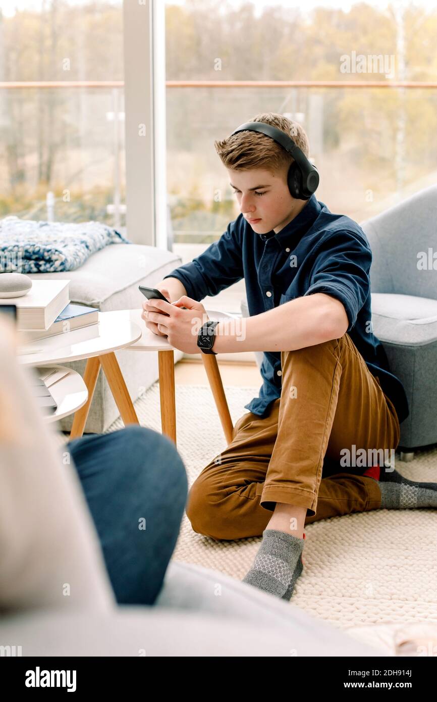 Teenager, der zu Hause auf dem Boden sitzt, mit dem Mobiltelefon Stockfoto