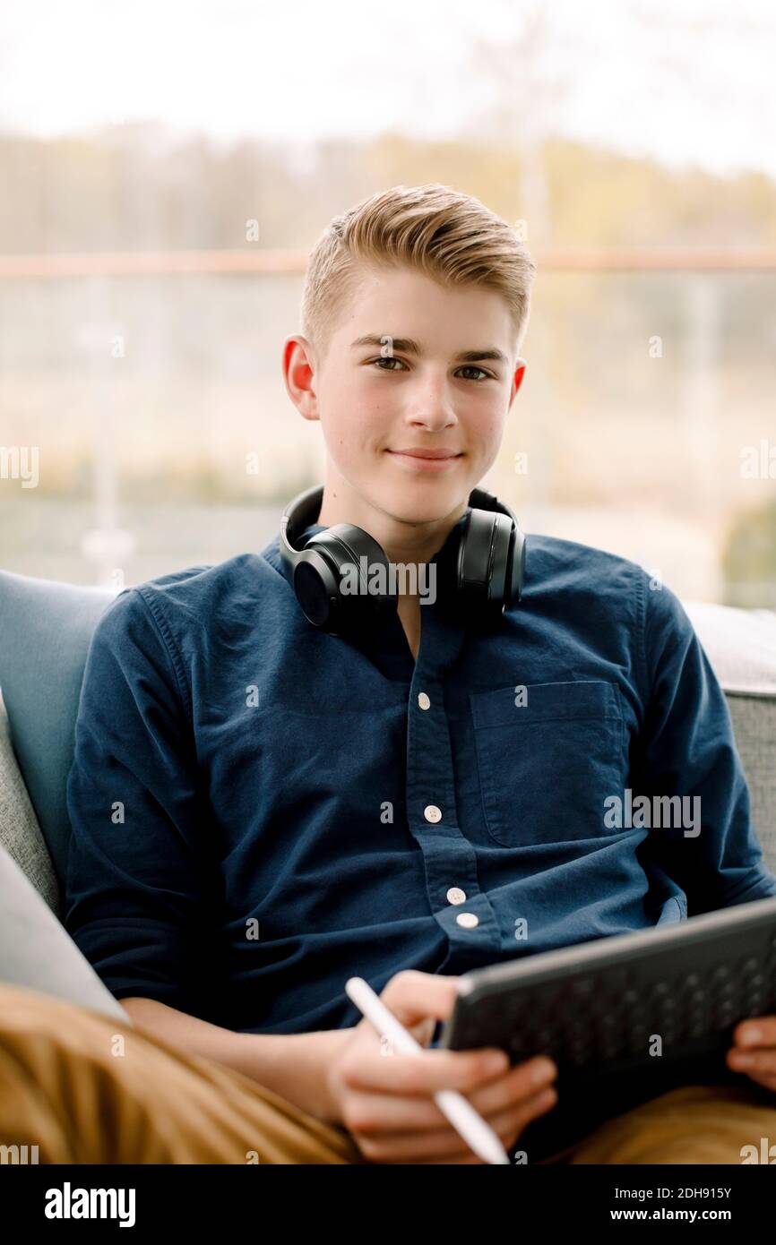 Porträt eines lächelnden Jungen im Teenageralter mit digitalem Tablet auf dem Sofa Zu Hause Stockfoto