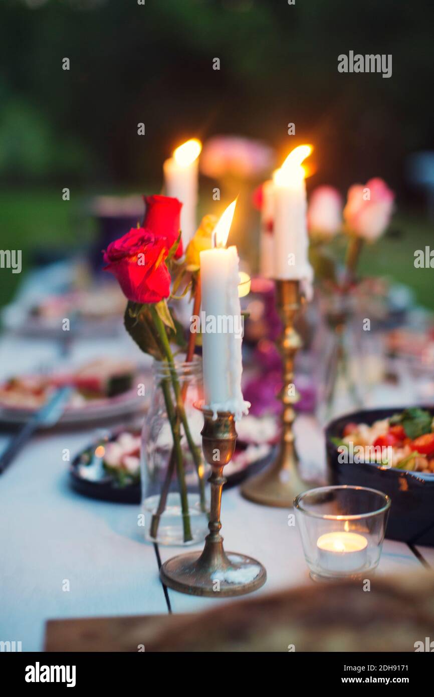 Rosen in Vase und entzündete Kerzen inmitten von Essen auf dem Tisch Bei Gartenparty Stockfoto