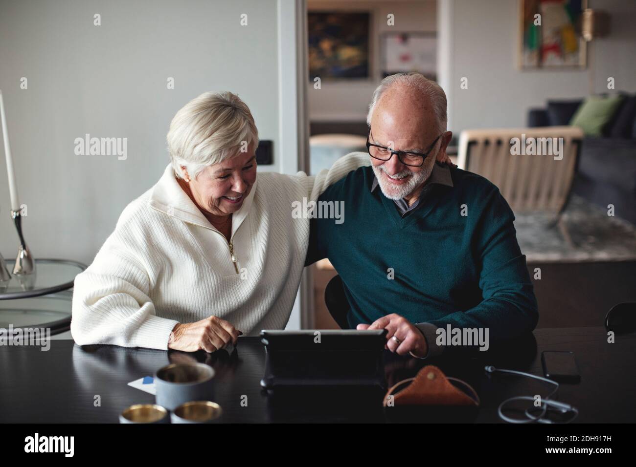 Lächelndes Seniorenpaar mit digitalem Tablet beim Essen Tisch im Wohnzimmer Stockfoto