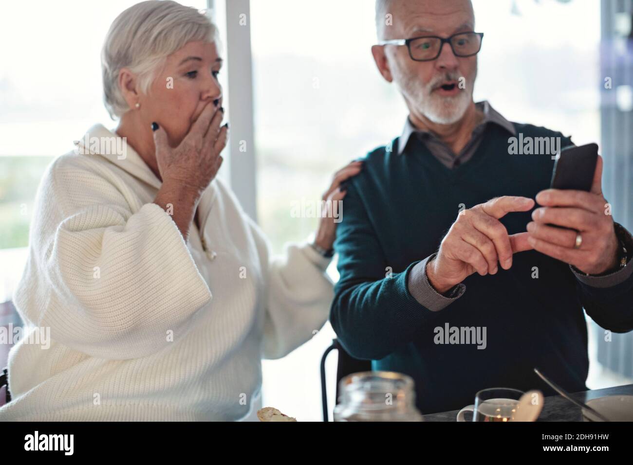 Schockiert Senior Pärchen mit Smartphone, während im Leben sitzen Zimmer Stockfoto