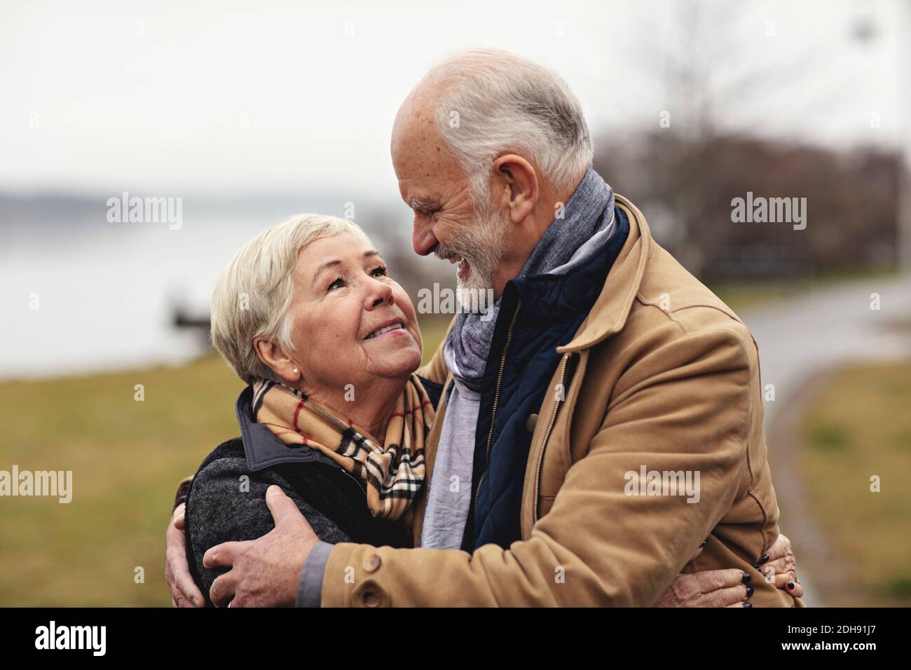 Lächelndes Seniorenpaar umarmt sich am See Stockfoto