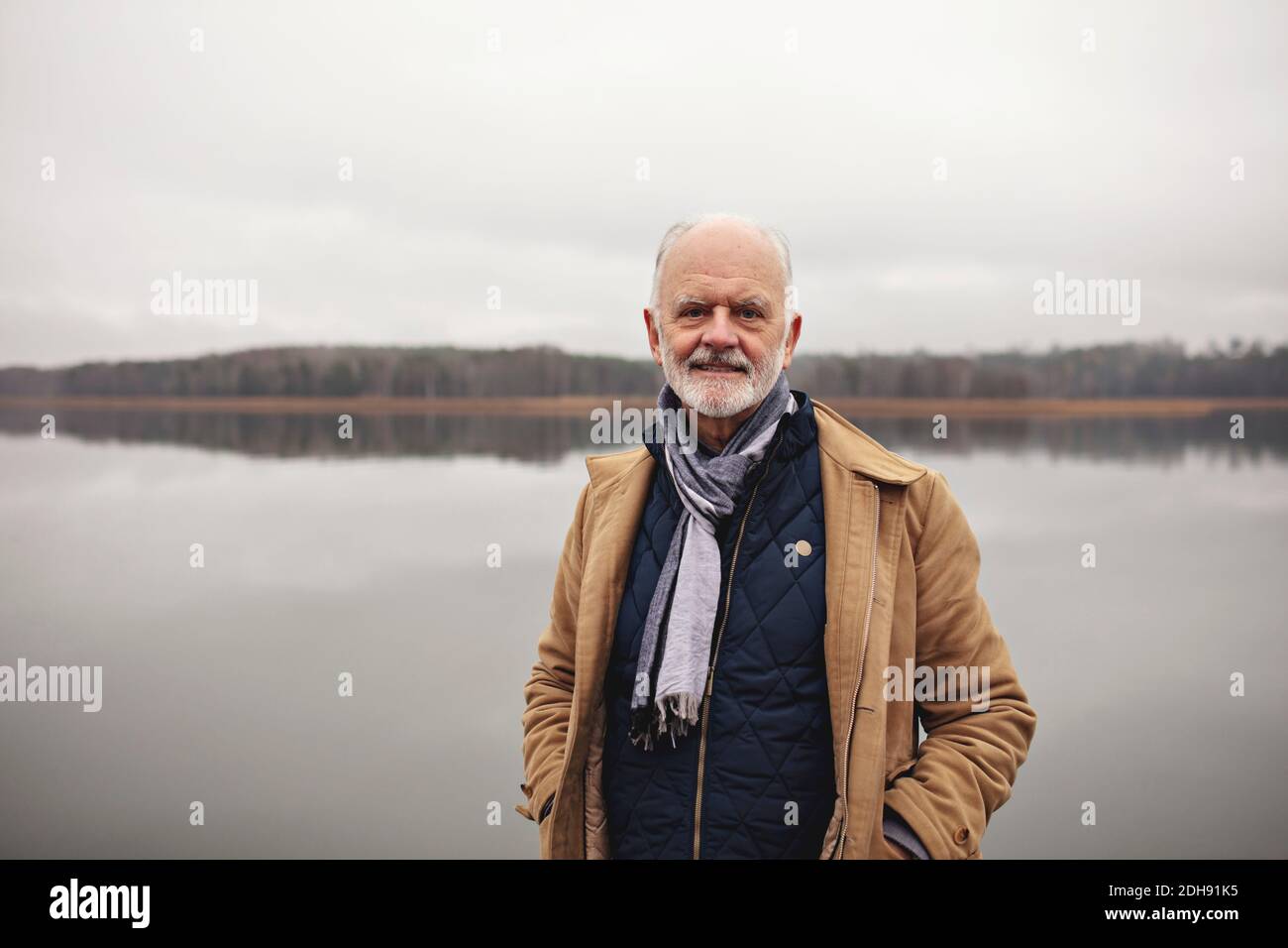 Porträt eines lächelnden älteren Mannes mit Händen in den Taschen stehen Am See Stockfoto