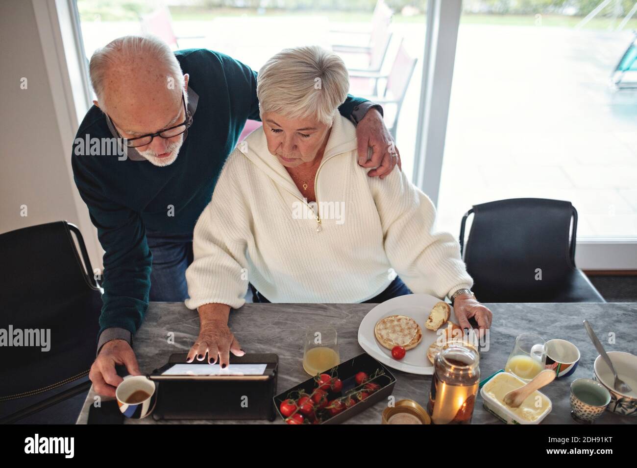 High-Angle-Ansicht des älteren Ehepaars, das digitale Tablets betrachtet Während Sie am Esstisch im Wohnzimmer sitzen Stockfoto