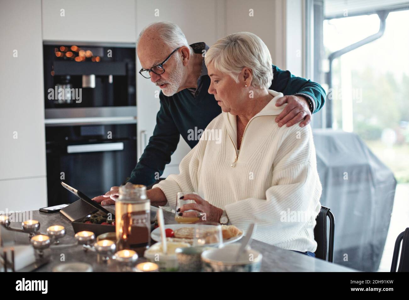 Ältere Paare, die beim Essen auf ein digitales Tablet schauen Tisch im Wohnzimmer Stockfoto