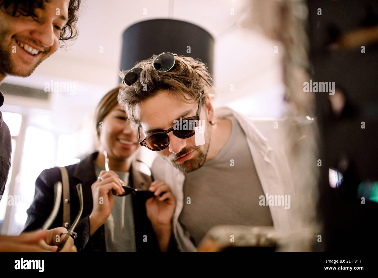 Lächelnder Mann versucht modische Brillen mit Freunden im Geschäft Stockfoto