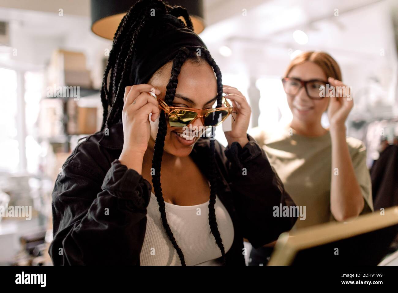 Lächelnde Freundinnen versuchen Brillen, während sie im Modeladen reden Stockfoto