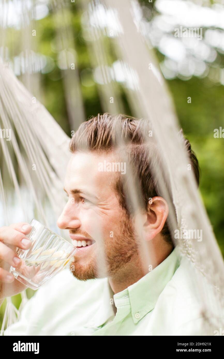 Lächelnder Mann trinkt, während er in der Hängematte ruht Stockfoto