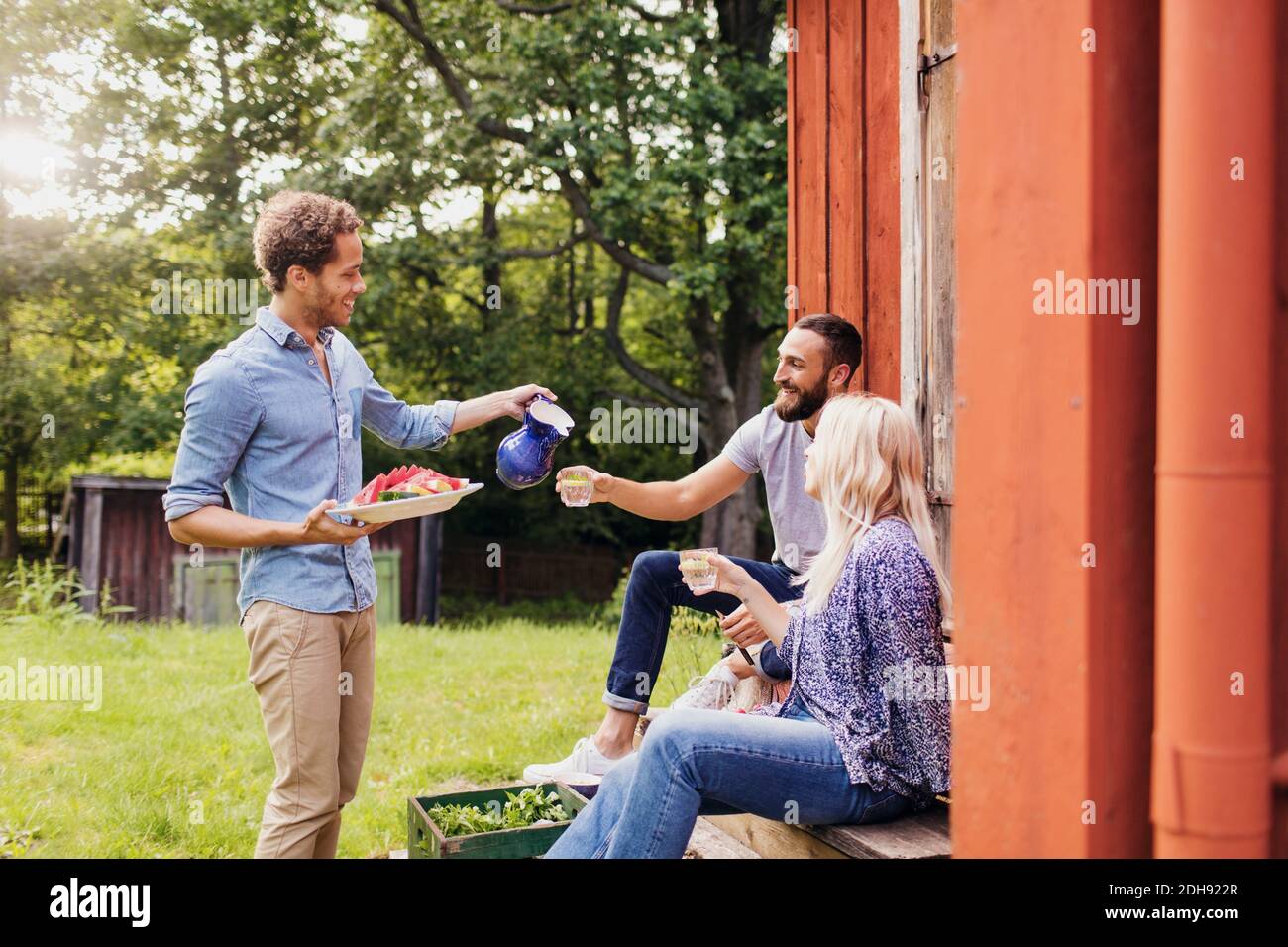 Mann hält Salattablett, während man den Freunden Getränke serviert Stockfoto
