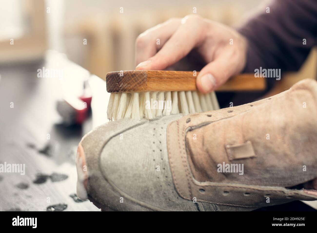 Sneaker aus Wildleder. Ein Arbeiter in einer Schuhwerkstatt reinigt einen Haufen Schuhe. Stockfoto