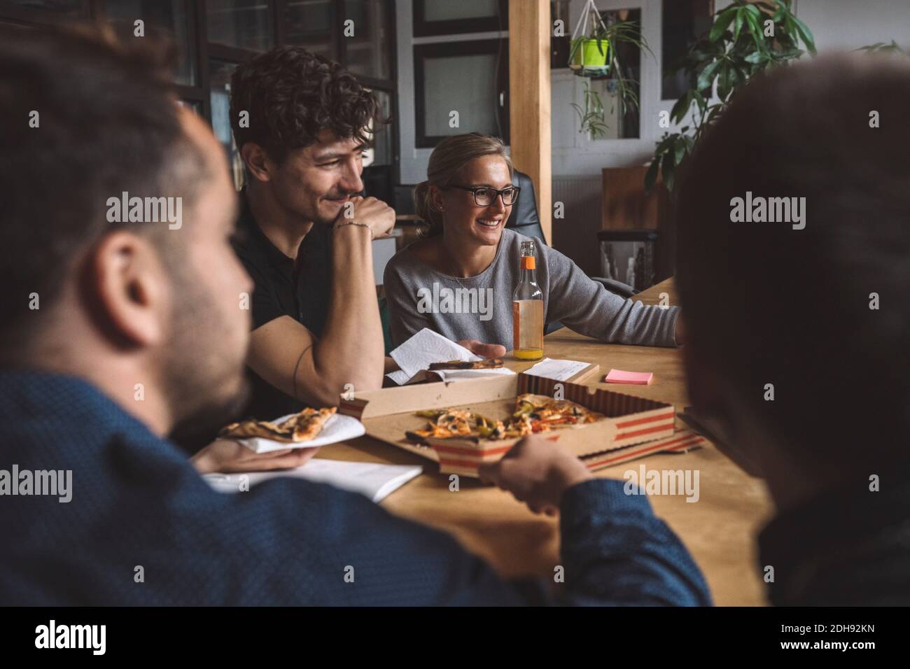 Lächelnde Kollegen essen Pizza am Arbeitsplatz Stockfoto