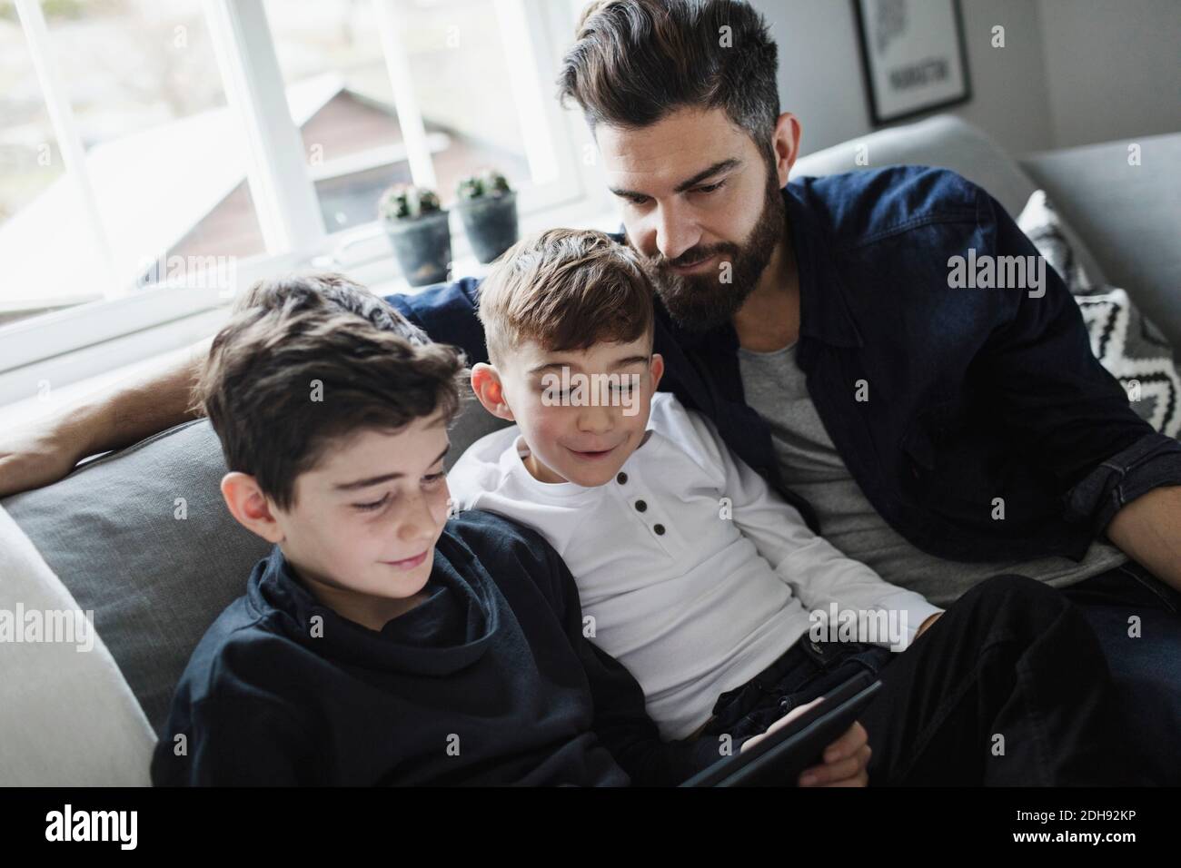 Tilt Schuss von Vater und Sohn Blick auf Junge mit Digitales Tablet im Wohnzimmer Stockfoto