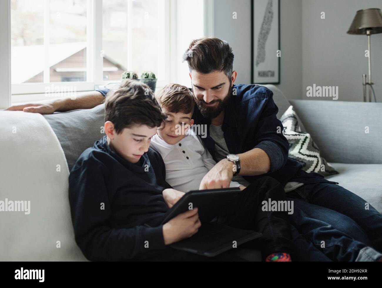 Vater und Söhne mit Tablet, während sie auf dem Sofa sitzen Zu Hause Stockfoto