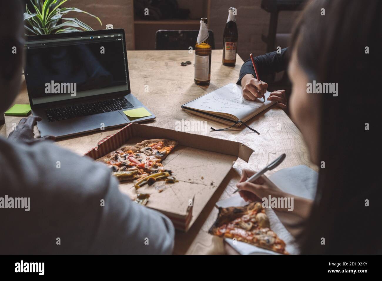 Mitarbeiter, die beim Essen von Pizza am Arbeitsplatz über die Codierung arbeiten Stockfoto