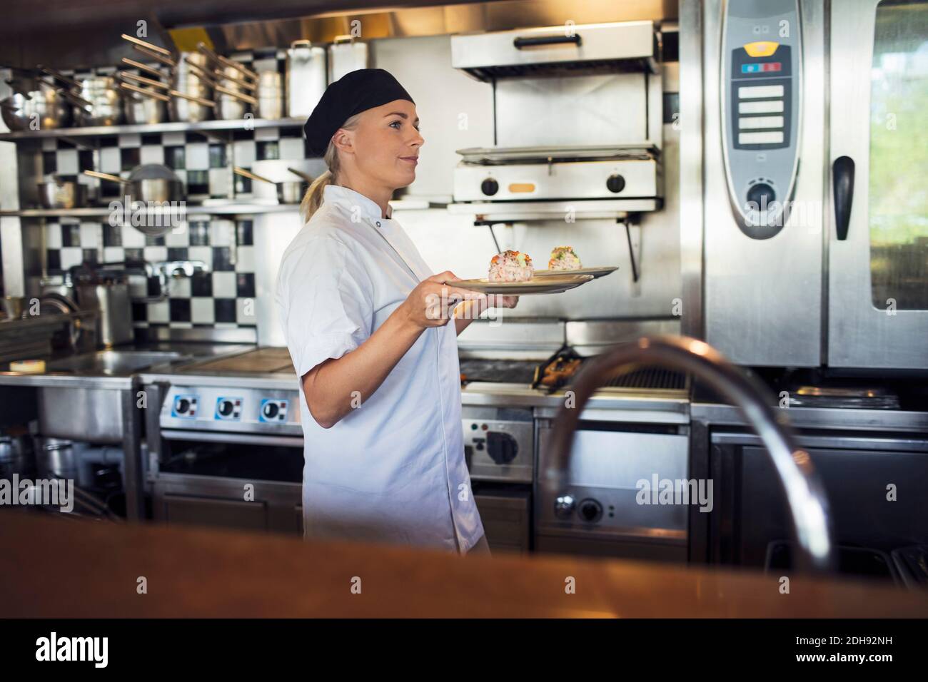 Weibliche Köchin serviert Essen in der Küche im Restaurant Stockfoto