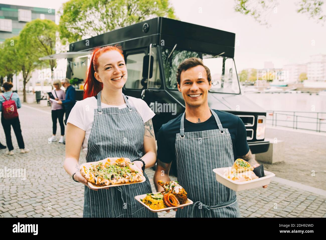 Lächelnder Besitzer mit Assistent hält indischen Teller in der Stadt Stockfoto