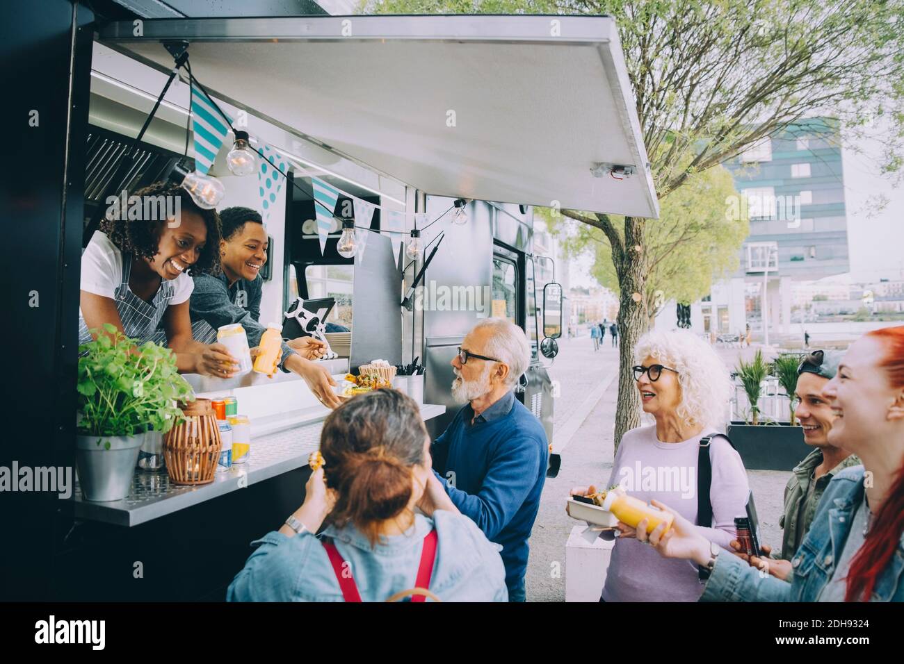 Lächelnde männliche und weibliche Kunden, die mit den Besitzern von Food-Trucks sprechen In der Stadt Stockfoto