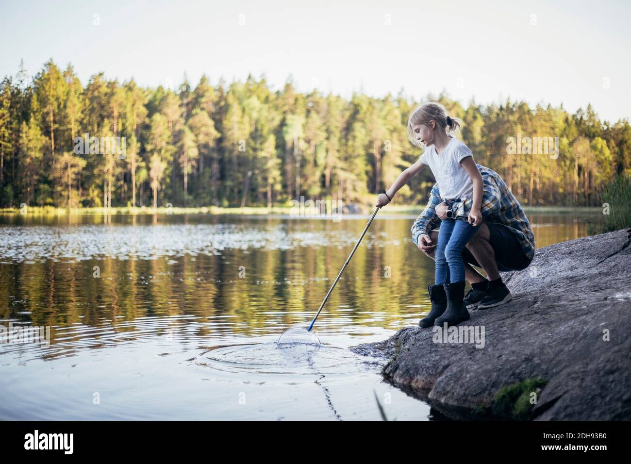 Vater hält Tochter während des Fischens beim Crouching am See Stockfoto