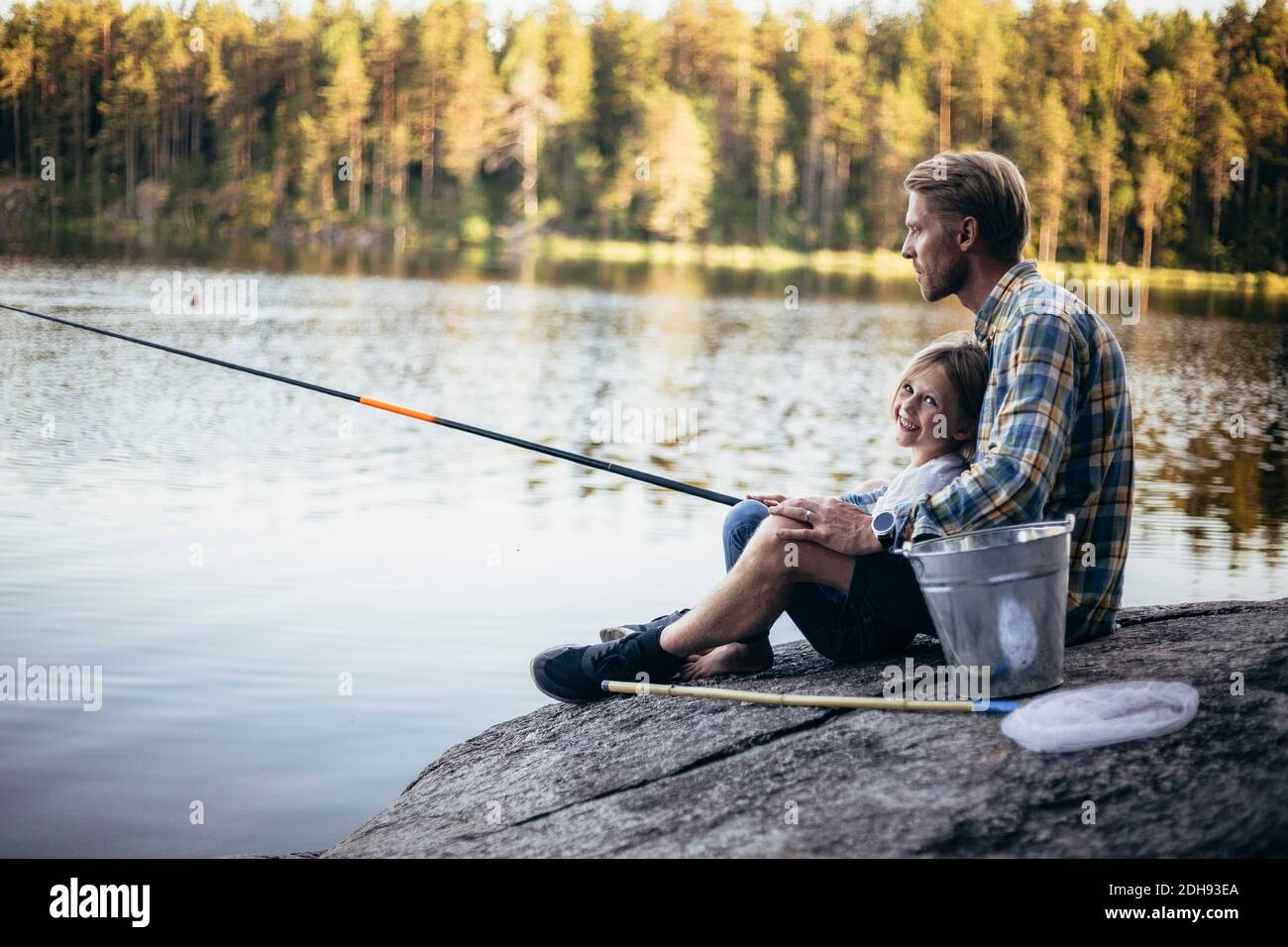 Portrait der lächelnden Tochter, die mit dem Vater angeln, während sie beim Sitzen sitzt see Stockfoto