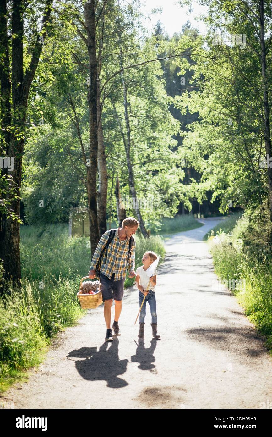 Tochter im Gespräch mit Vater hält Picknickkorb auf der Straße in Wald Stockfoto