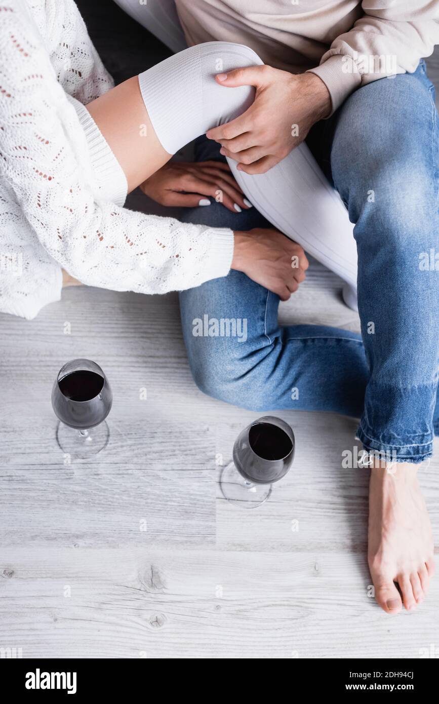 High-Winkel-Ansicht der barfuß Mann berühren Bein der Freundin In Kniestrumpfen neben Gläsern Wein auf dem Boden Stockfoto