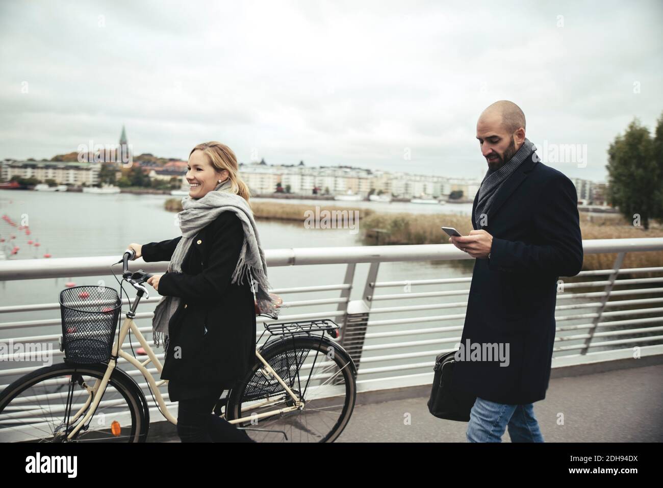 Lächelnde Geschäftsfrau mit Fahrrad zu Fuß von Geschäftsmann auf der Brücke Stockfoto