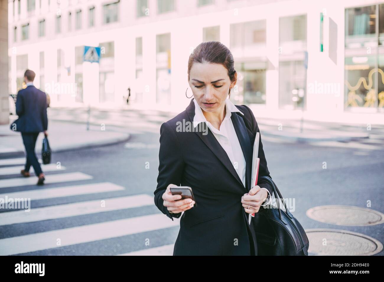 Geschäftsfrau, die Smartphone beim Überqueren der Straße in der Stadt betrachtet Stockfoto