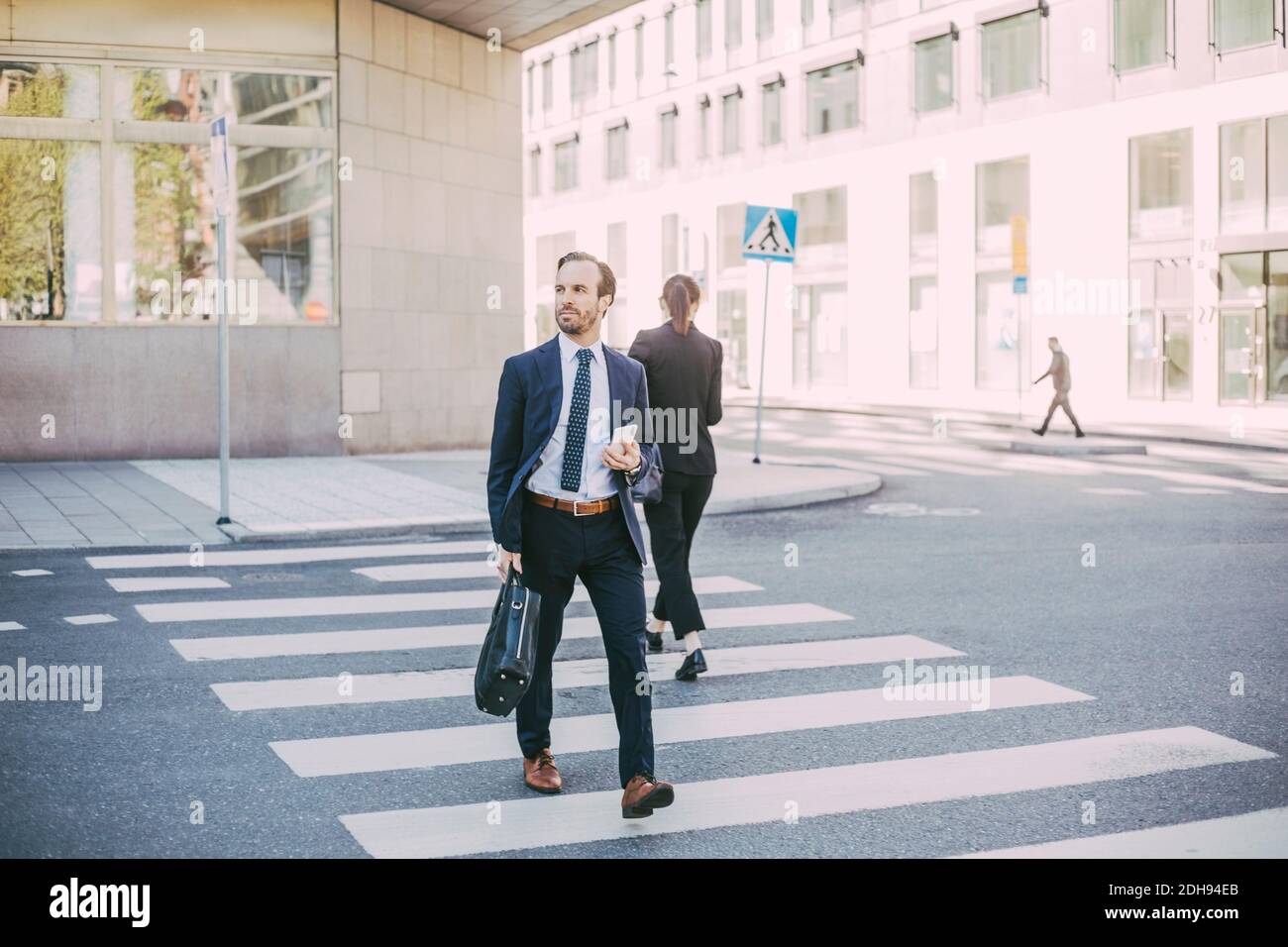 Geschäftsmann mit Telefon schaut weg, während er die Straße in der Stadt überquert Stockfoto