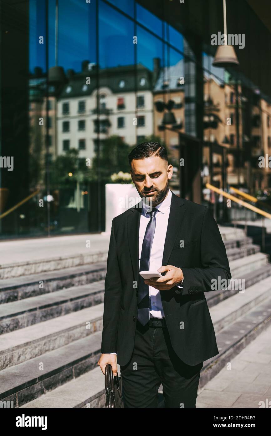 Geschäftsmann, der Smartphone benutzt, während er in der Stadt läuft Stockfoto