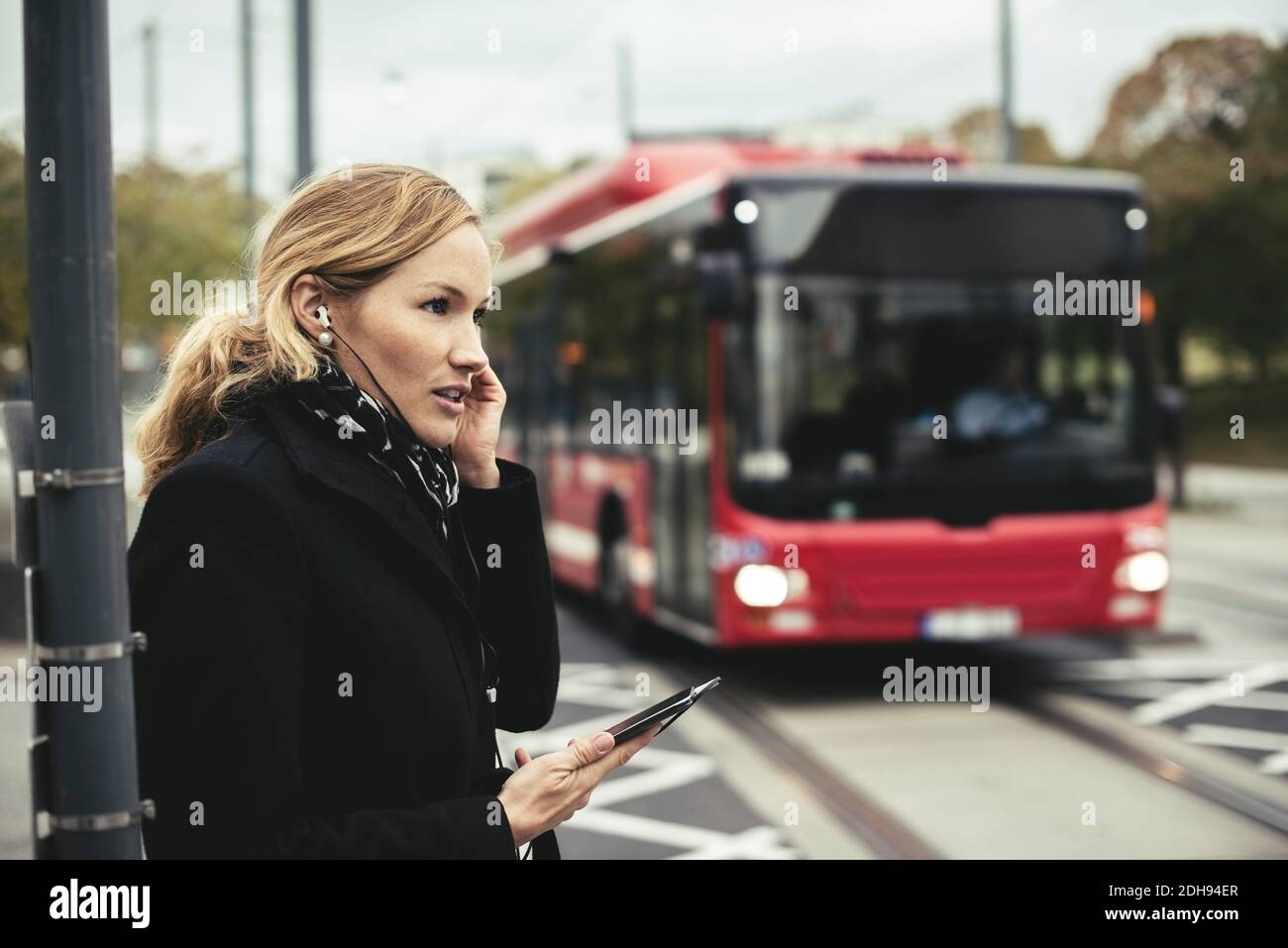 Seitenansicht einer Geschäftsfrau, die mit dem Bus auf dem Mobiltelefon spricht Im Hintergrund Stockfoto