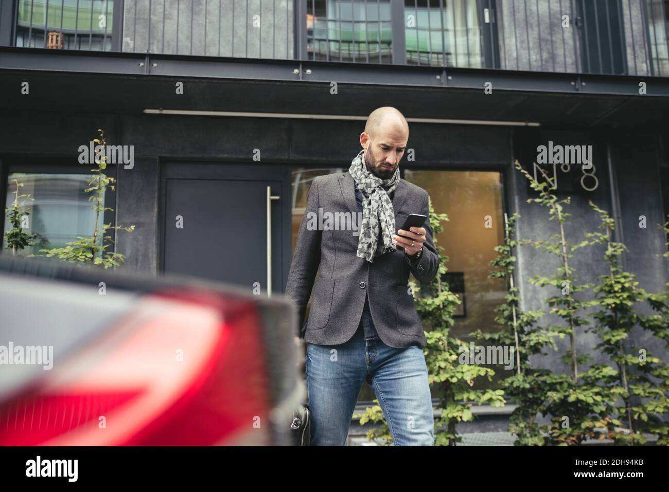 Mittelerwachsener Geschäftsmann, der Handy gegen Gebäude benutzt Stockfoto