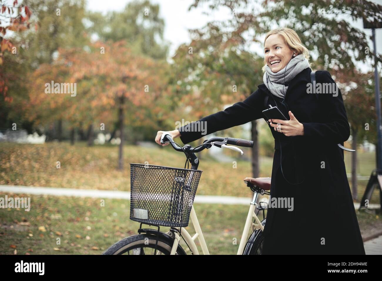 Lächelnde Geschäftsfrau, die im Herbst beim Spaziergang mit dem Fahrrad Musik genießt Stockfoto