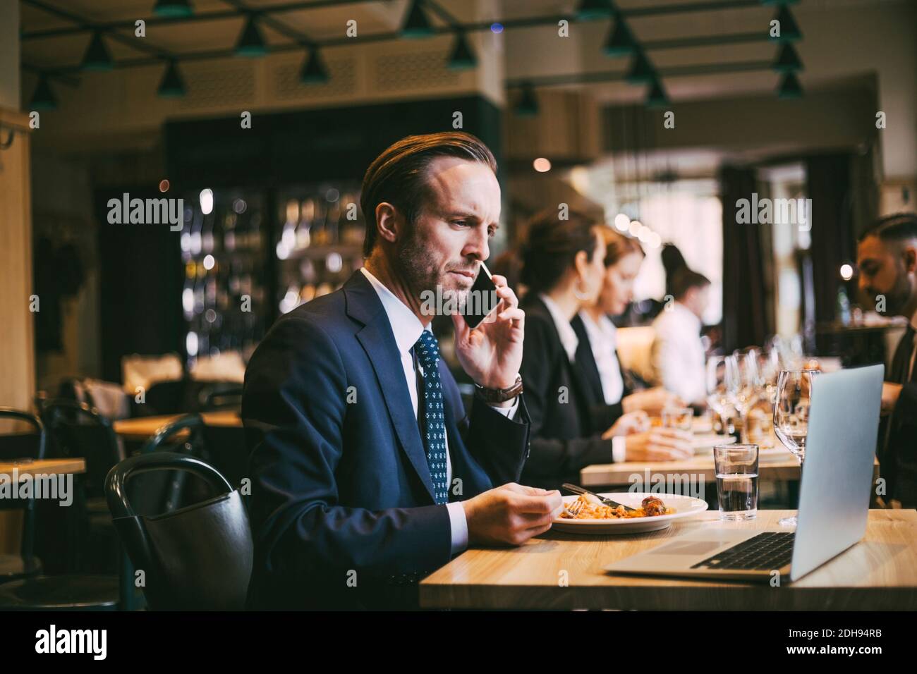 Männlicher Geschäftsmann, der am Telefon telefoniert, während er Essen isst Restaurant Stockfoto