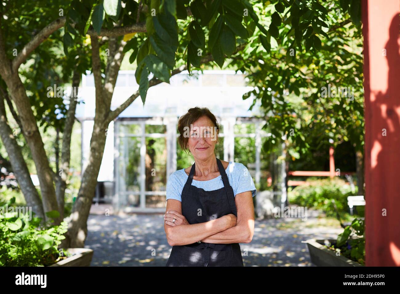 Porträt einer selbstbewussten Gärtnerin stehende Arme gekreuzt auf Hof Stockfoto