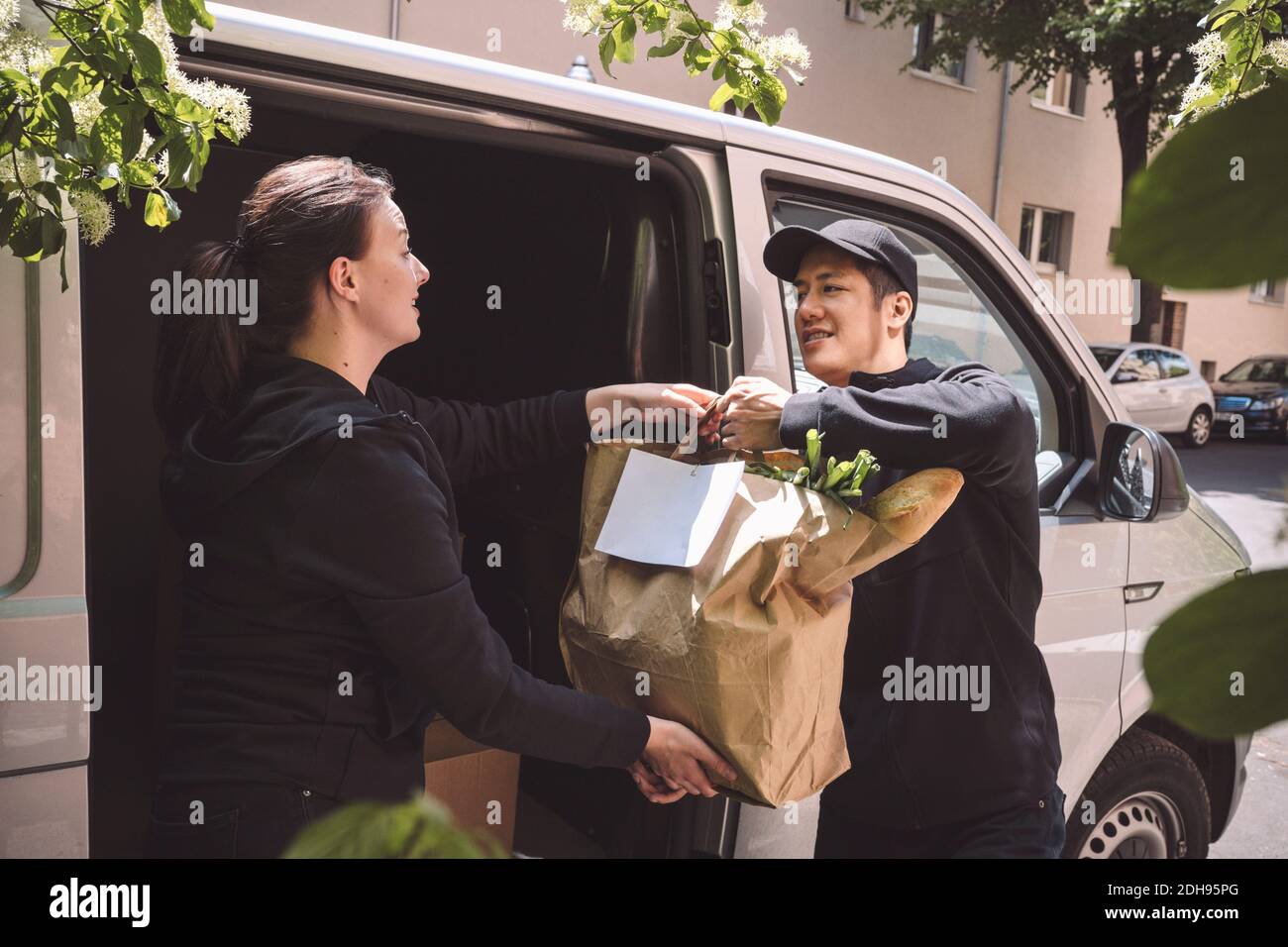 Delivery Mann im Gespräch mit weiblichen Kollegen, während die Verpackung Tasche halten In der Nähe des Staplers Stockfoto