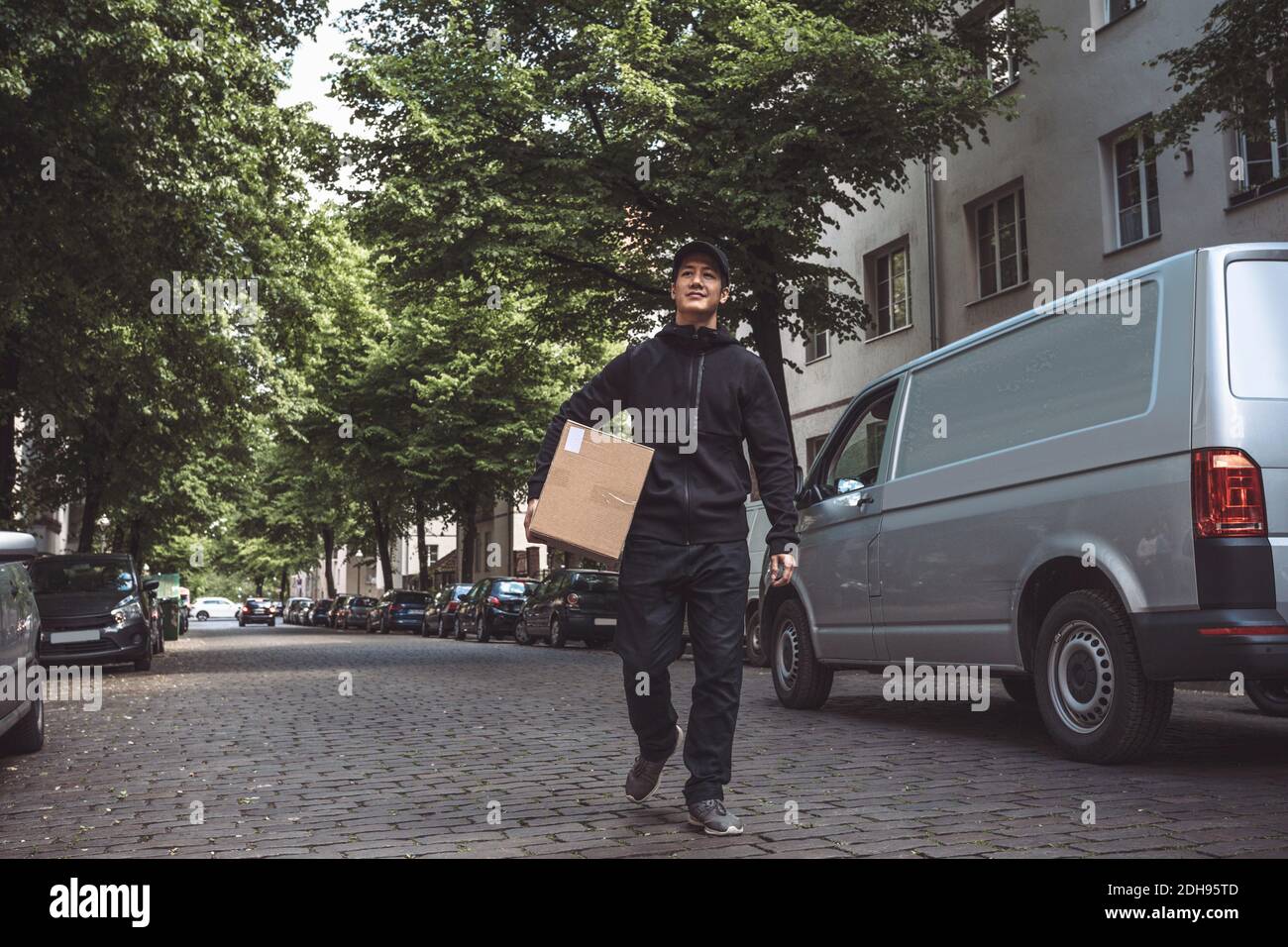 Selbstbewusster Lieferer mit Paket zu Fuß auf der Straße in der Stadt Stockfoto