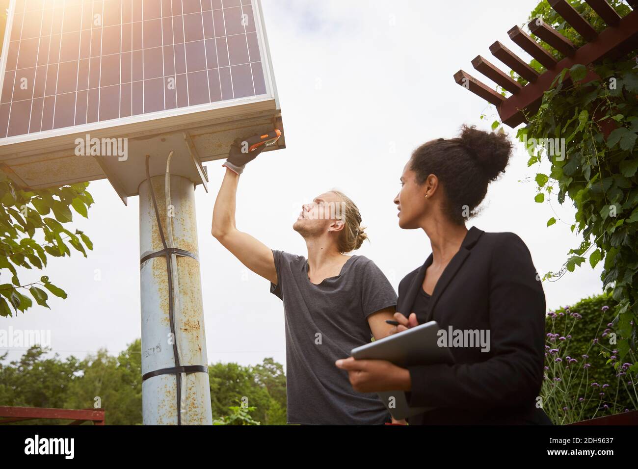 Low-Winkel-Ansicht des Gartenarchitekten Anpassung Solarpanel durch Kollege mit Tablet-Computer Stockfoto