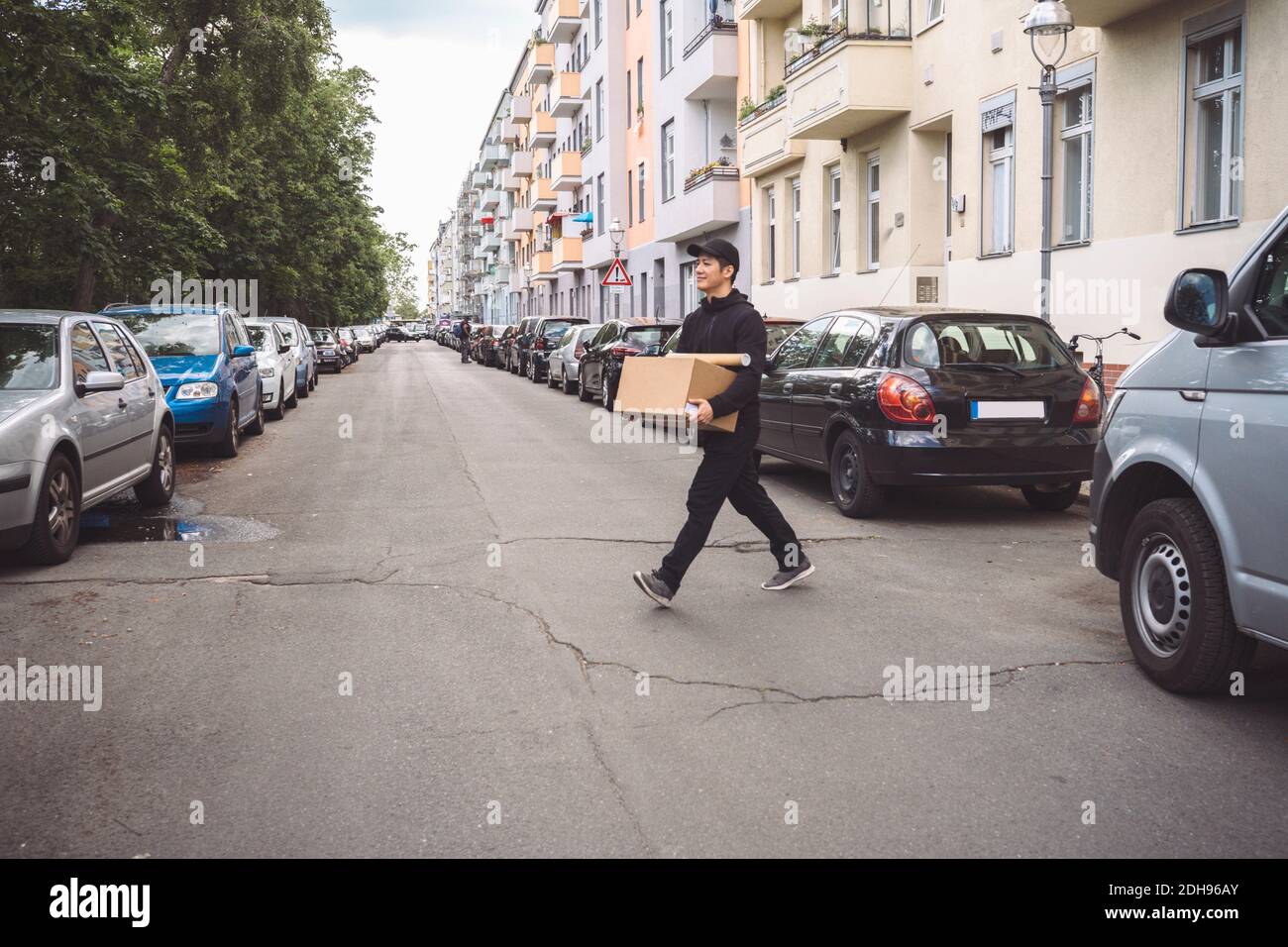Selbstbewusster Lieferer mit Pappkarton, der auf der Straße herkommt Stadt Stockfoto