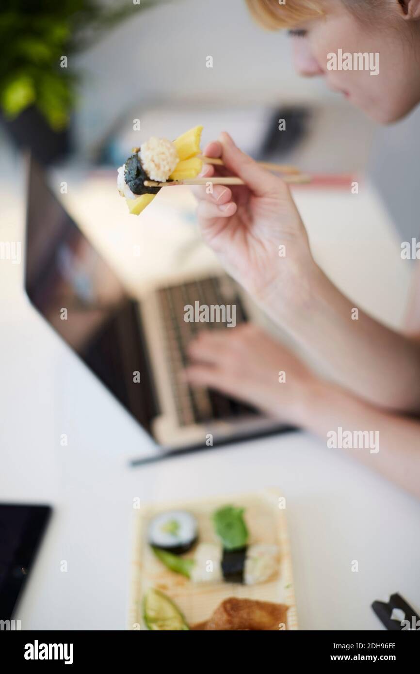 High-Angle-Ansicht der Geschäftsfrau mit Sushi während der Verwendung Laptop Am Tisch im Büro Stockfoto