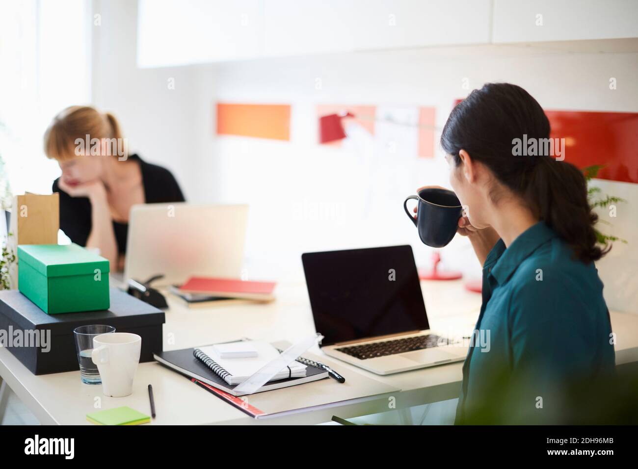 MittelErwachsene Geschäftsfrau trinkt Kaffee am Tisch mit weiblicher Kollegin Im Hintergrund im Büro Stockfoto