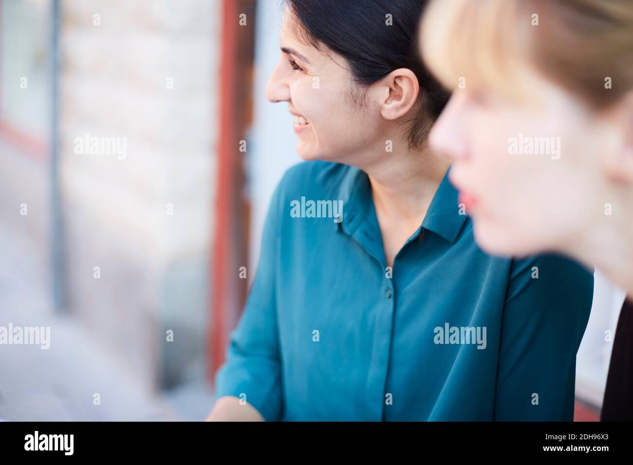 Lächelnde Geschäftsfrau mit mittlerem Erwachsenenalter und einer Kollegin, die nach draußen schaut Büro Stockfoto