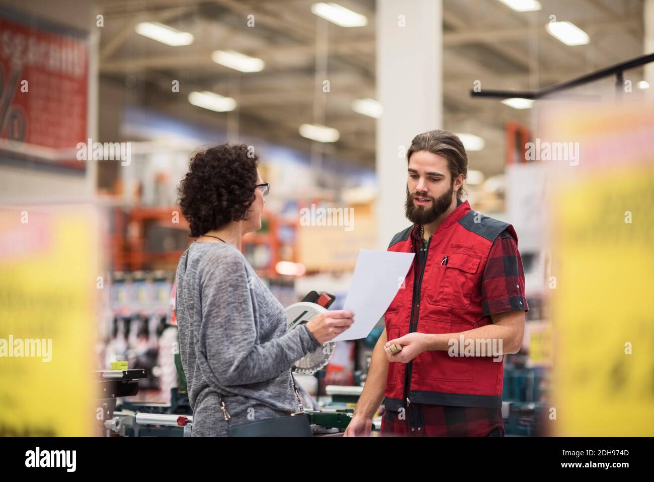 Verkäufer spricht mit weiblicher Kundin, die Dokument im Hardwareladen hält Stockfoto